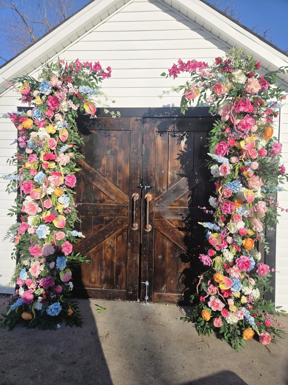 Tall floral columns of peonies, anthurium, hydrangea and bougainvillea framing barn doors