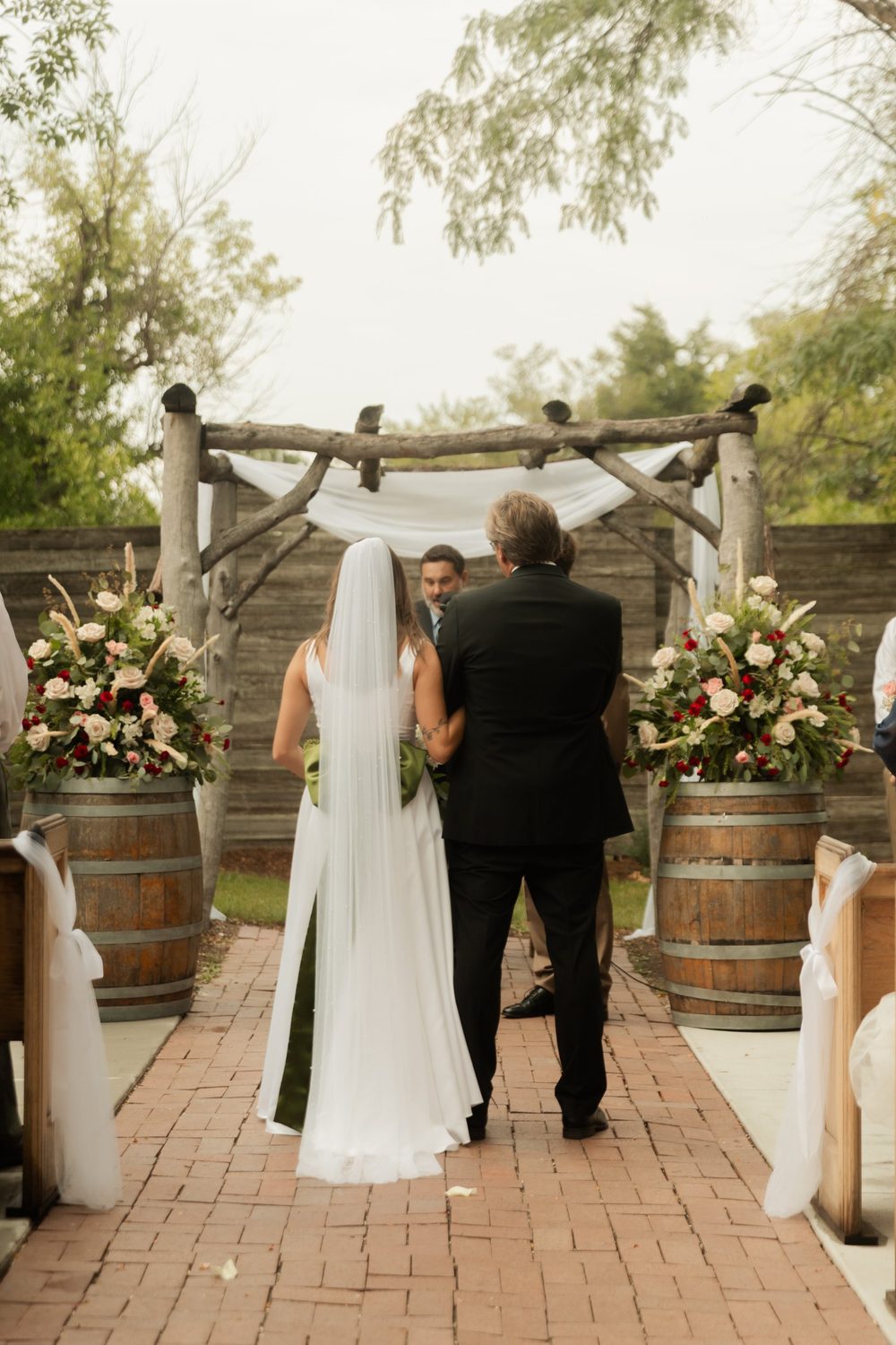 Tall arrangements of roses, carnations and pampas on barrels at the head of the aisle