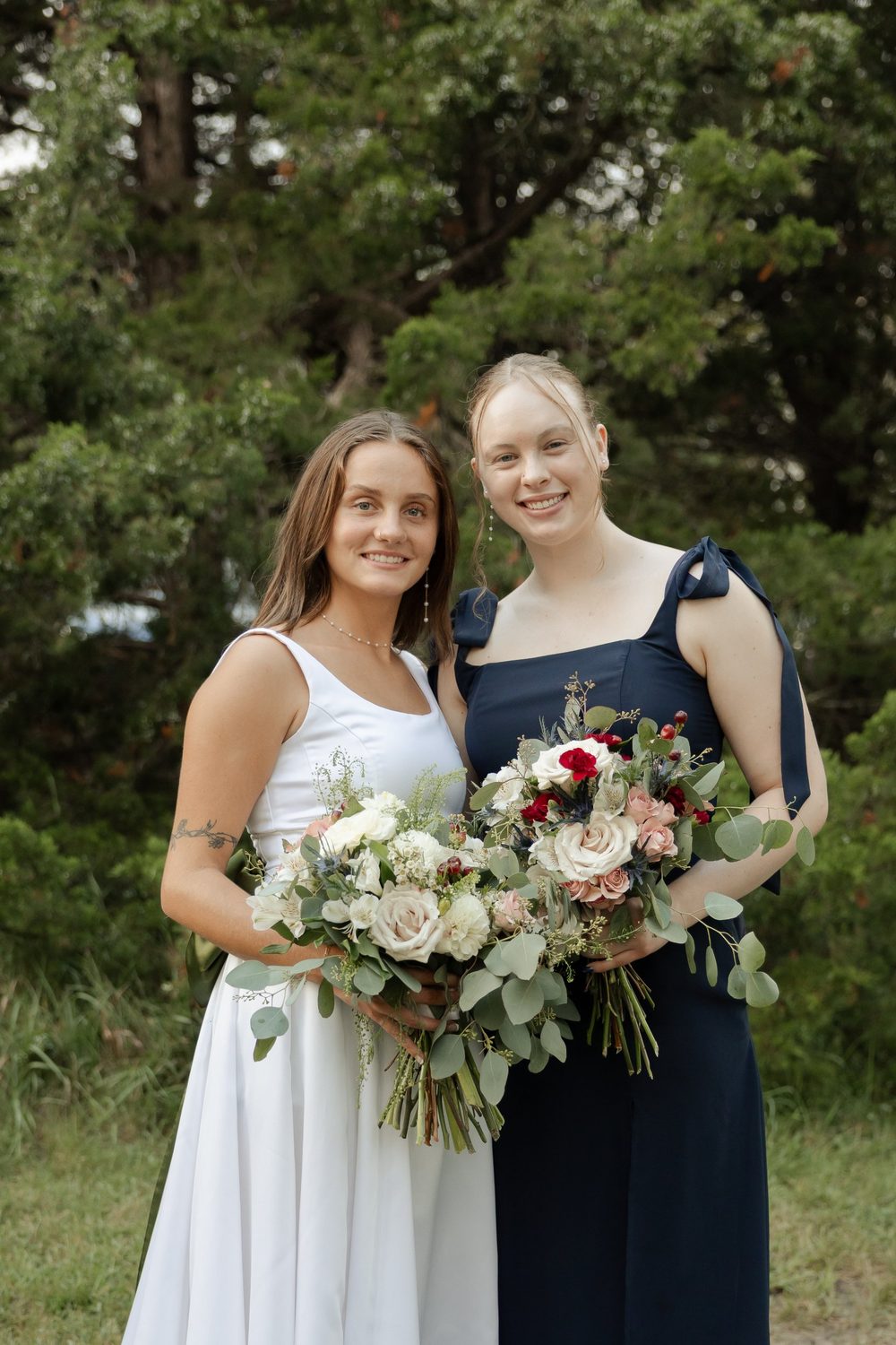 The bride’s bouquet beside a bridesmaid’s, with deep red carnations and blue thistle