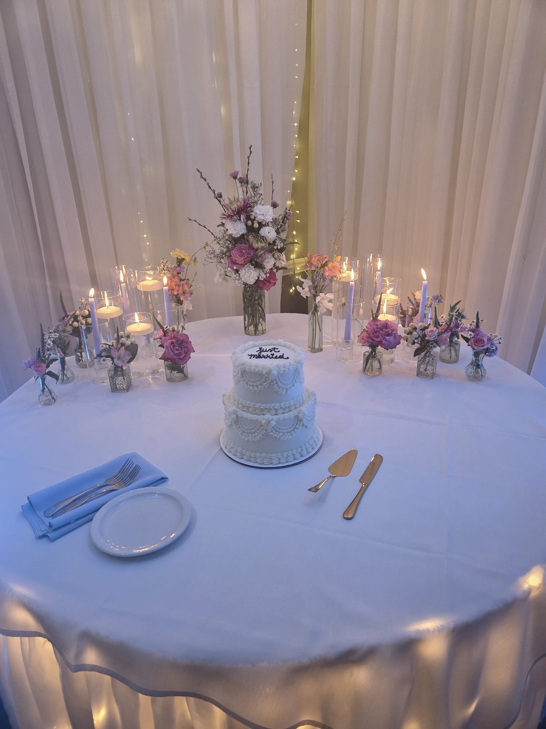 Bud vases of garden roses and wildflowers with candlelight around the wedding cake