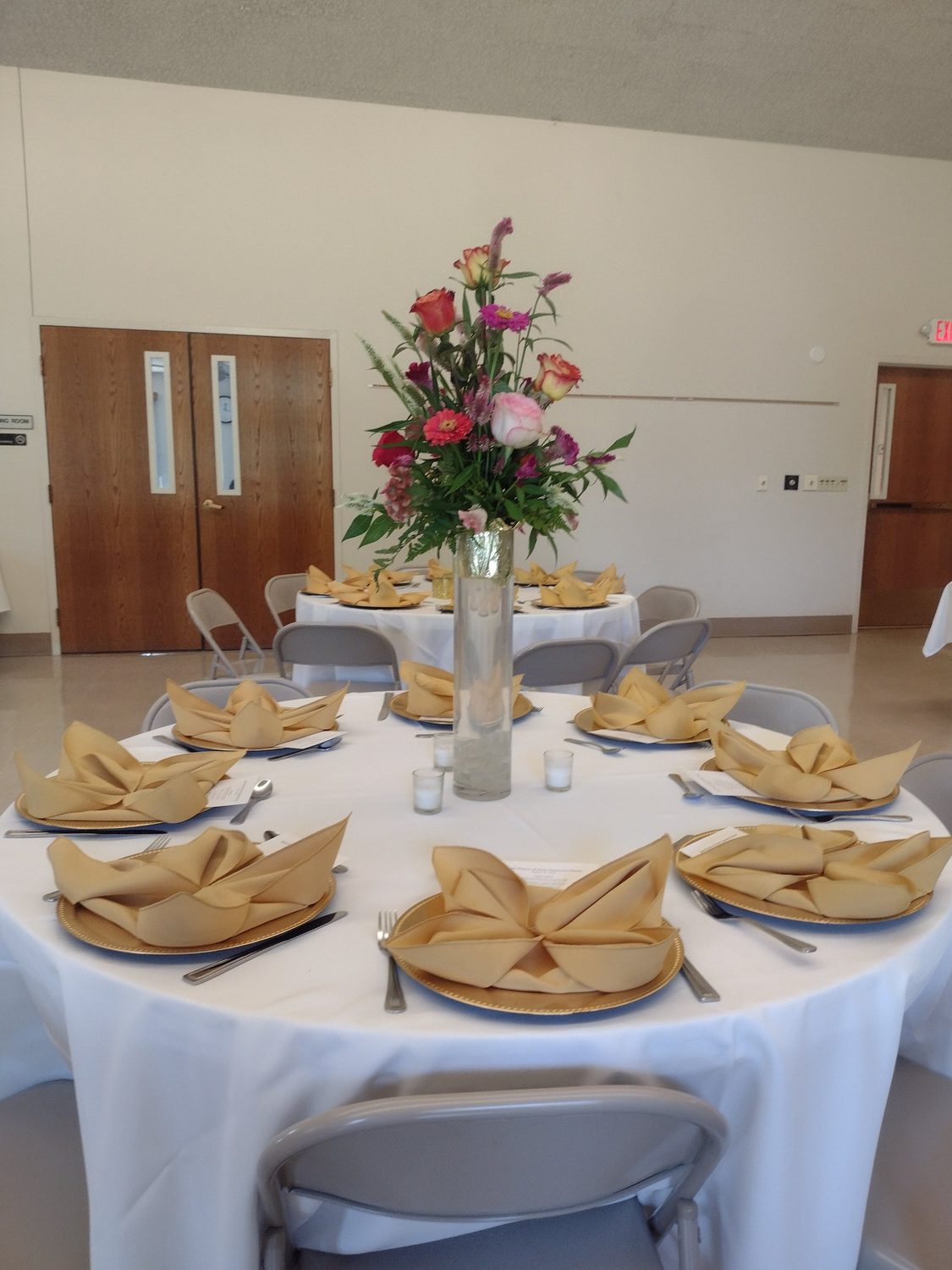 A tall centerpiece of roses, zinnias and celosia for a dinner with gold place settings
