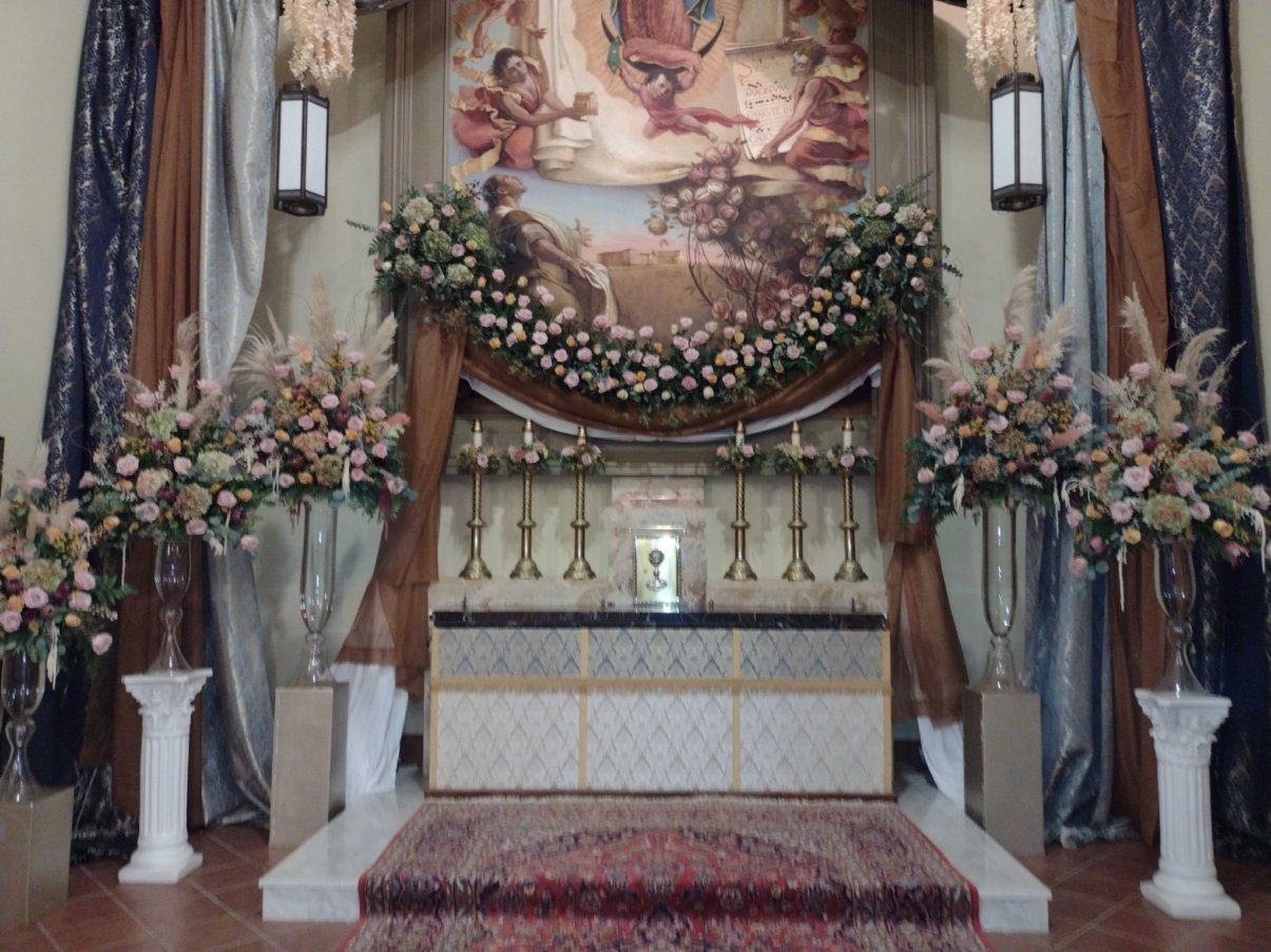 A rose garland and pampas urns framing the painting of Our Lady of Guadalupe