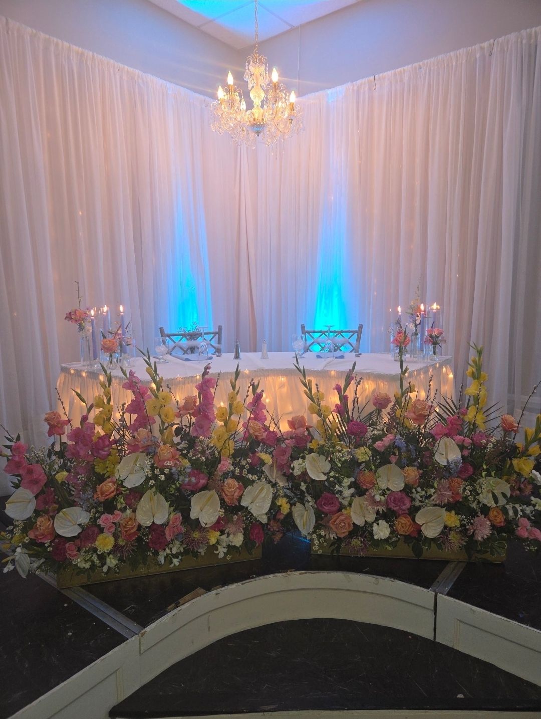 Low garden-style arrangements of gladiolus, roses and anthurium before the head table