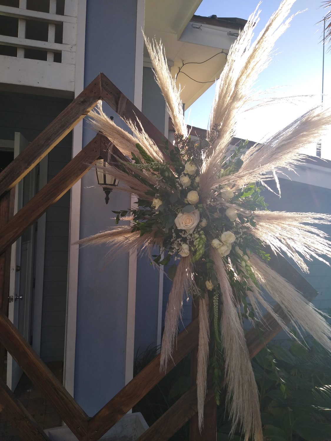 A burst of pampas grass, white roses and greenery on a geometric ceremony arch