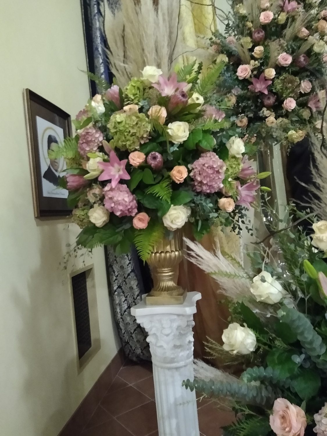 A pedestal urn of protea, hydrangea, lilies and roses