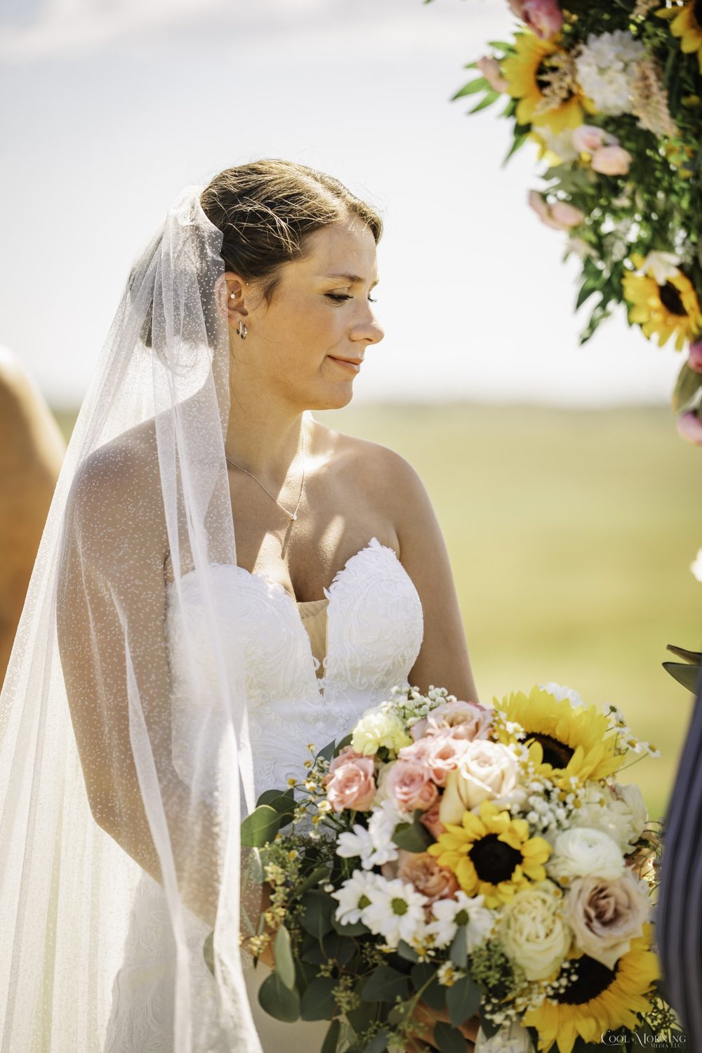 A hand-tied bouquet of sunflowers, blush roses, ranunculus and daisies