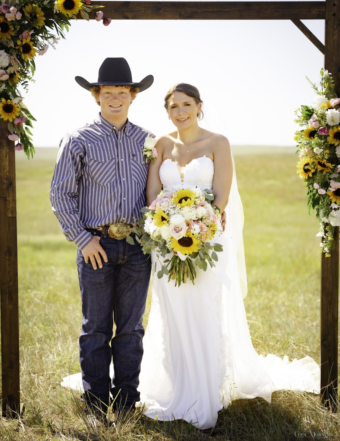 The bride and groom under the sunflower arch, his boutonniere matched to her bouquet