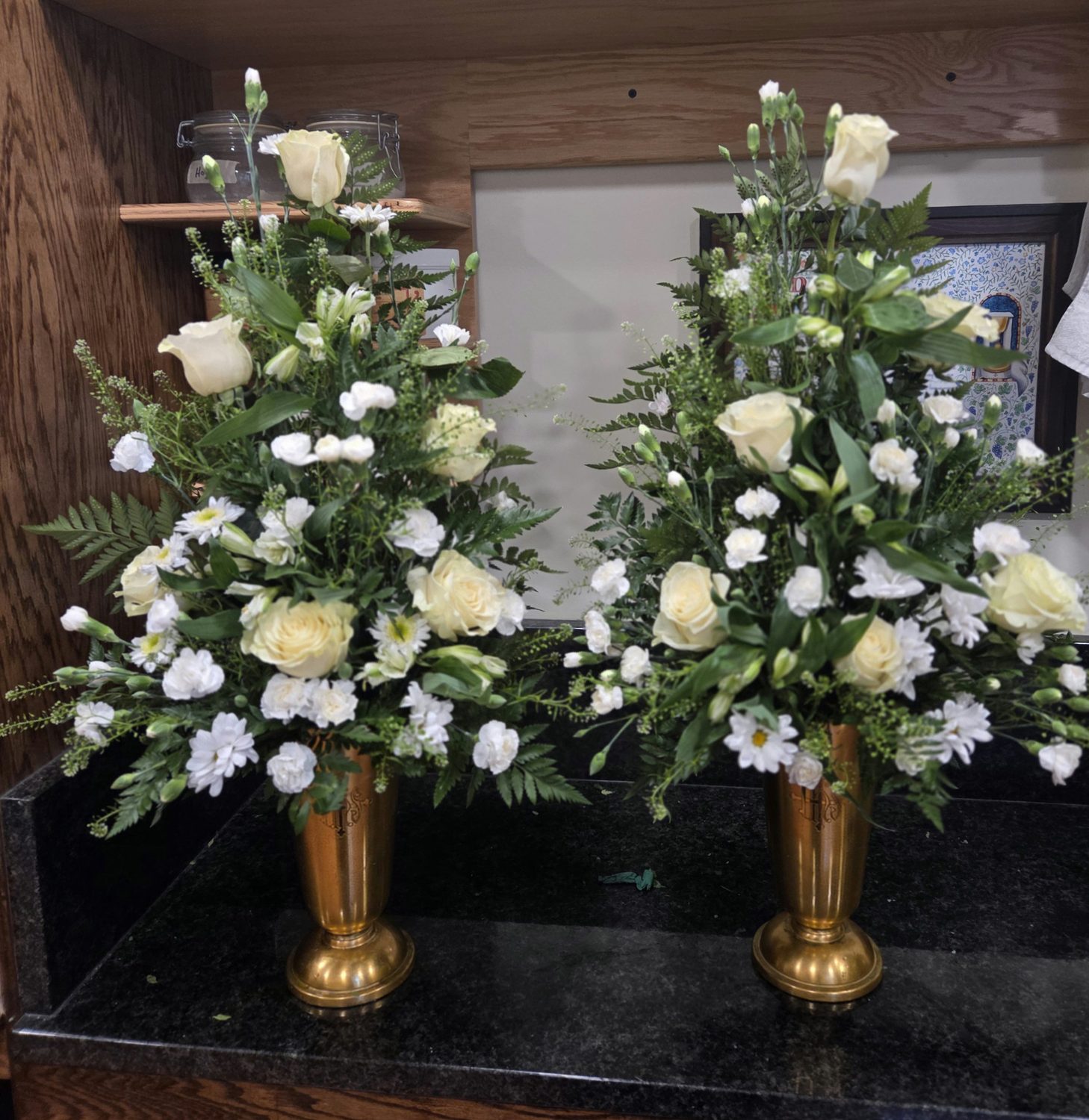 A pair of white altar arrangements of roses, carnations and daisies in brass vases